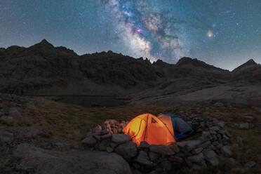 Scenic view of tent on lake shore against snowy mountain under cloudy milky way sky in evening located in Circo de Gredos cirque in Spain - ADSF31878