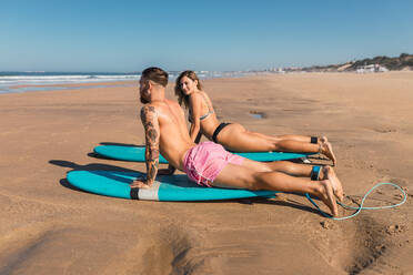 Ganzkörper-Seitenansicht von Sportlern in Badekleidung, die auf Surfbrettern liegen und sich auf das Surfen am Sandstrand in einem tropischen Ferienort vorbereiten - ADSF31882