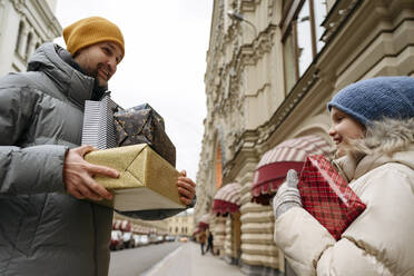 Smiling father and daughter holding Christmas gifts at city street - EYAF01810