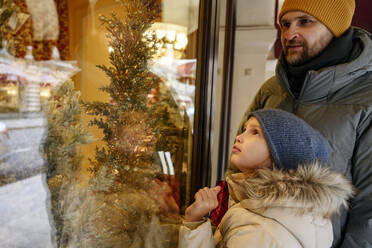 Vater beim Schaufensterbummel unter dem Weihnachtsbaum mit Tochter im Geschäft - EYAF01814