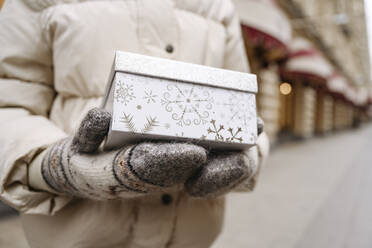 Mädchen mit Wollhandschuh und Weihnachtsgeschenk auf dem Fußweg - EYAF01819