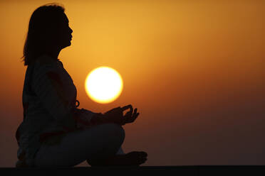 Frau übt Yoga-Pose und Meditation bei Sonnenuntergang als Konzept für Ruhe und Entspannung, Vereinigte Arabische Emirate, Naher Osten - RHPLF20797