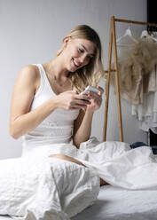 Smiling woman text messaging through smart phone on bed - JBYF00038