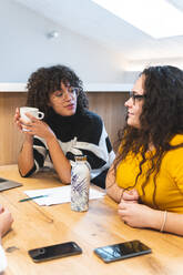 Businesswoman with coffee mug discussing with colleague at office - JAQF01000