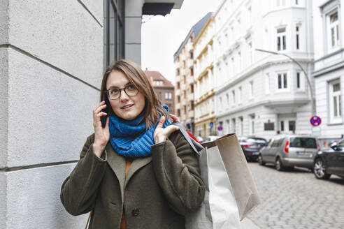 Frau mit Einkaufstüten, die an der Wand mit einem Mobiltelefon spricht - IHF00605