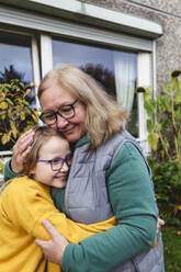 Lächelnde Großmutter umarmt Enkelin im Hinterhof - IHF00609