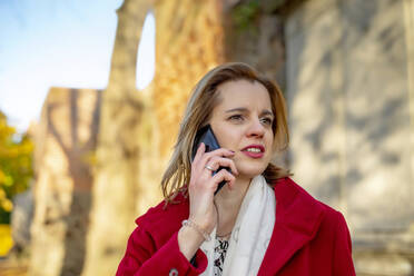 Woman with jacket talking on smart phone at autumn - BFRF02386