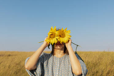 Frau bedeckt Gesicht mit Sonnenblumen an einem sonnigen Tag - TYF00059