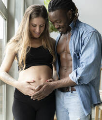 Glückliches Paar, das ein Baby erwartet, betrachtet den Bauch einer schwangeren Frau zu Hause - JCCMF04652