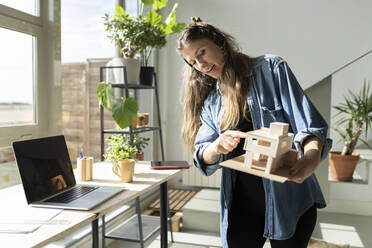 Architect pointing at model on video conference at home office - JCCMF04668