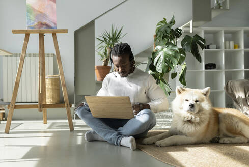 Kundendienstmitarbeiter arbeitet am Laptop neben einem Hund auf dem Boden zu Hause - JCCMF04674