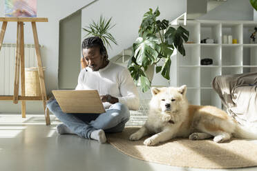 Kundenbetreuerin mit Laptop neben einem Hund im Wohnzimmer - JCCMF04675