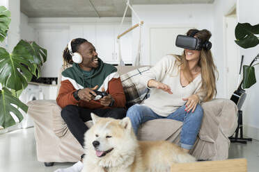 Fröhliches Paar spielt Videospiel vor dem Hund zu Hause - JCCMF04686