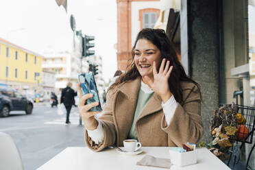 Happy young woman on video call through smart phone at sidewalk cafe - MEUF04798