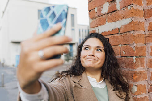 Junge Frau macht Gesicht, während sie ein Selfie mit ihrem Smartphone macht - MEUF04802