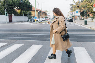 Plus size woman using smart phone while crossing road - MEUF04808