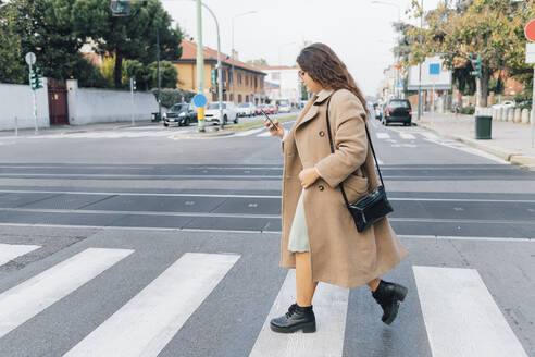 Frau mit Übergröße benutzt Smartphone beim Überqueren der Straße - MEUF04808