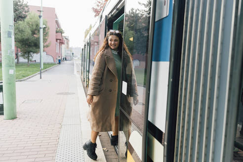 Lächelnde, wegschauende Frau beim Einsteigen in eine Straßenbahn - MEUF04809