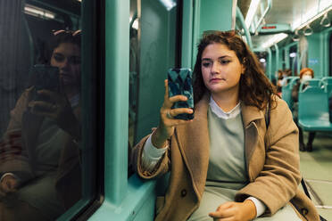 Junge kurvige Frau benutzt Smartphone in öffentlichen Verkehrsmitteln - MEUF04831