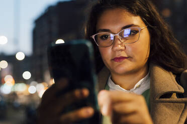 Junge Frau mit Brille, die ein Mobiltelefon benutzt - MEUF04840