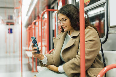 Young curvy woman in eyeglasses using mobile phone in train - MEUF04845
