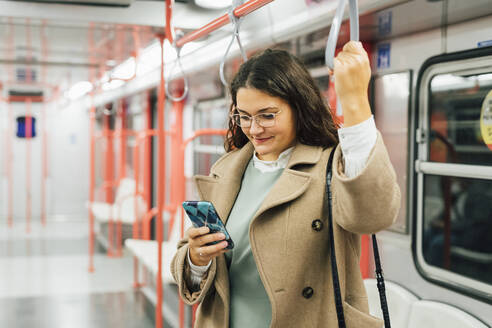 Lächelnde junge Frau mit Übergröße, die ein Mobiltelefon im Zug benutzt - MEUF04846