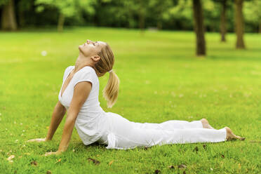 Young flexible woman practicing cobra pose in park - MOMF00961