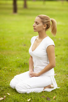 Blond woman with eyes closed meditating in park - MOMF00963