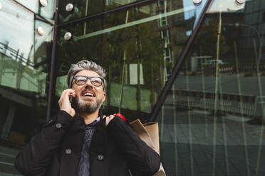 Businessman with shopping bags talking on smart phone - IHF00627