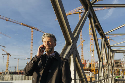 Bärtiger Geschäftsmann spricht auf einer Brücke mit seinem Smartphone - IHF00631