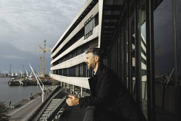 Geschäftsmann mit verschränkten Händen und Blick auf die Elbe, Hafencity, Hamburg, Deutschland - IHF00649