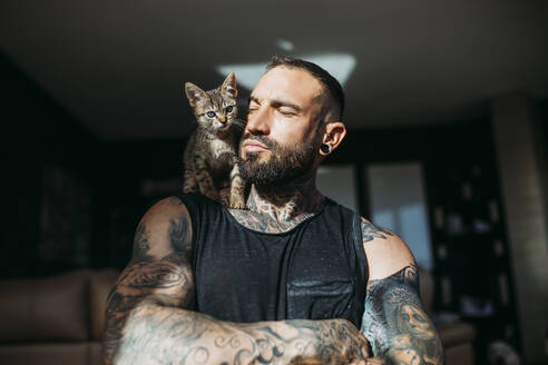 Mixed breed cat sitting on muscular man's shoulder at home - MIMFF00728