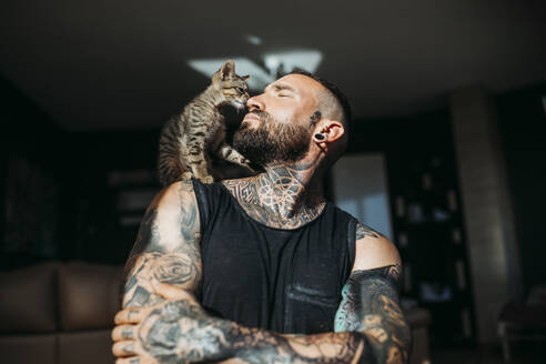 Mann mit verschränkten Armen schaut auf eine Katze, die auf der Schulter sitzt - MIMFF00730