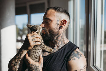 Mann mit Tattoo küsst Katze zu Hause - MIMFF00731