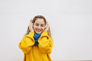 Lächelnde Frau mit geschlossenen Augen hört Musik vor weißem Hintergrund - IHF00654