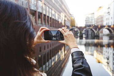 Woman photographing Ellerntorsbrucke bridge through mobile phone at canal - IHF00681