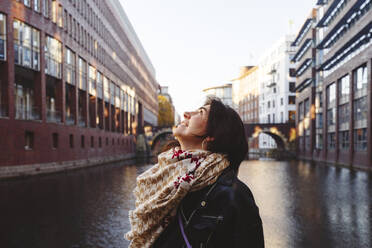 Thoughtful woman wearing scarf and jacket at canal - IHF00683