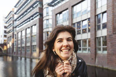 Smiling woman holding scarf at canal - IHF00684