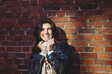 Happy woman with scarf in front of brick wall - IHF00689