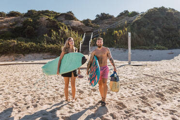 Full body of happy sportive couple with surfboards strolling together on sandy beach before training in the sea - ADSF31888