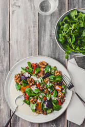 Draufsicht auf einen leckeren Salat mit Linsen und Gemüse, garniert mit Walnüssen, serviert auf einem weißen Teller neben einer Schale mit Basilikumblättern - ADSF31893