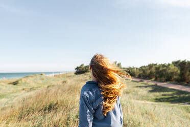 Back view of unrecognizable young female in casual outfit standing on grassy meadow in summer looking at camera - ADSF31916