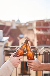 Unbekannte junge Freunde stoßen mit Bierflaschen an, während sie gemeinsam auf der Terrasse chillen - ADSF31970