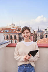 Positive young female in casual clothes standing with tablet on balcony - ADSF31984