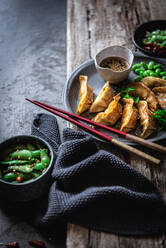 Gyozas with green beans and soy sauce with sesame seeds placed with chopsticks near bowls with spices and pea pods - ADSF32049