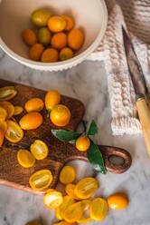 Top view pile of fresh orange cut kumquats on wooden chopping board placed on marble table with towel in kitchen - ADSF32051