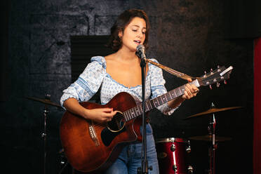 Selbstbewusste Dame mit Gitarre singt in Mikrofon während der Durchführung Song in hellen Club - ADSF32076