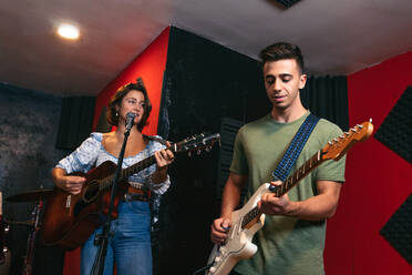 Positiver junger Mann spielt Gitarre in der Nähe einer Musikerin, die akustische Gitarre spielt und in einem hellen Club singt - ADSF32079