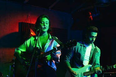 Mann spielt Gitarre, während eine Frau singt und ein Lied in einem Club mit Neonlichtern vorträgt - ADSF32080