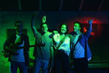 Eine Band verabschiedet sich nach einem Konzert mit Gitarren und Schlagzeug vom Publikum, während eine Frau in einem Club mit Neonlichtern singt und ein Lied vorträgt - ADSF32089
